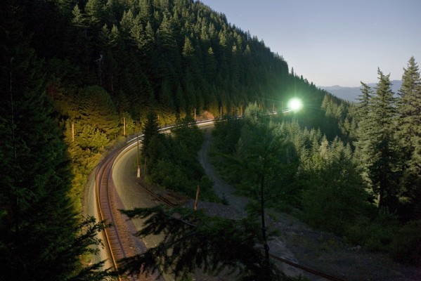 Rear locomotive of Union Pacific's Portland to Roseville freight train (QPDRV) making a trail of lights between tunnels 7 and 6 at Cruzatte, Oregon, while a signal glows green in the distance.