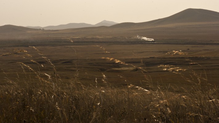 Westbound Jitong Railway freight train steaming through the windswept fields near Lindong, Inner Mongolia, China.