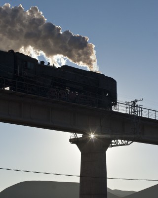 The morning sun silhouettes the Jitong Railway's bridge at Reshui, Inner Mongolia, China, on a November 2005 morning as a westbound passenger special crosses.