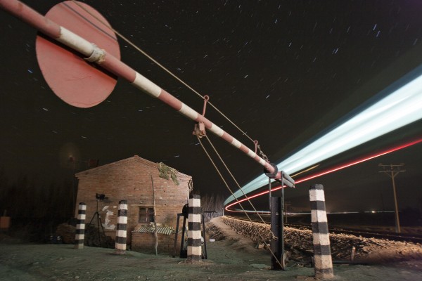 On a fall night in 2005, the Jitong Railway's streamlined diesel passenger train passes a rural road crossing near Gulumanhan, Inner Mongolia, China.