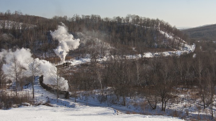 Two narrow-gauge 0-8-0 C2 steam locomotives pull and push an eight-car loaded coal train up the steep grade west of Lixin, Heilongjiang, China, on November 30, 2005.