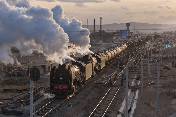 Two QJ steam locomotives lead a Jitong Railway freight train out of Daban, Inner Mongolia, China, at sunset on a November day in 2005. Workers are busier extending the tracks of the Daban yard to accommodate the longer trains that will result when diesels takeover in the following month.