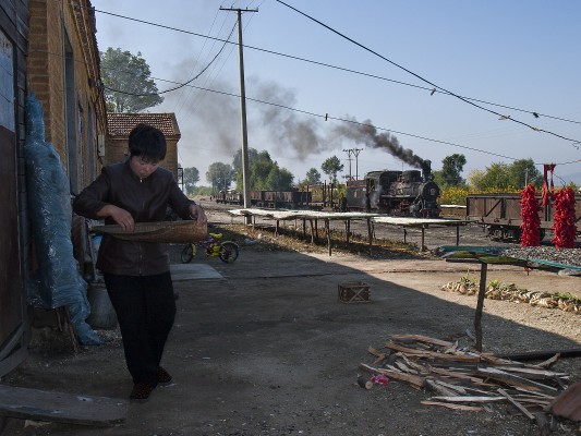 A woman in the village of Xiahua carries a wicker basket for pumpkin seeds as a short train on the narrow-gauge Huanan Forestry Railway passes in the background on September 27, 2005.