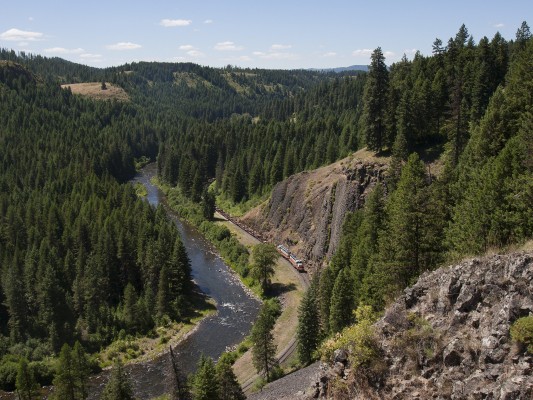On a hot July afternoon in 2005, the St. Maries River Railroad's outbound Clarkia Logger rolls past basalt cliffs along its namesake near milepost 17 of the branch line running south from St. Maries, Idaho.
