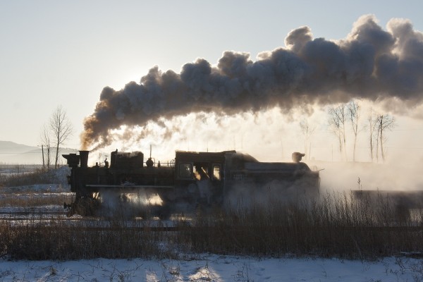 The morning sun silhouettes a narrow-gauge 0-8-0 C2 steam locomotive of the Huanan Forestry Railway leaving the village of Xiahua on a cold November morning in 2005.