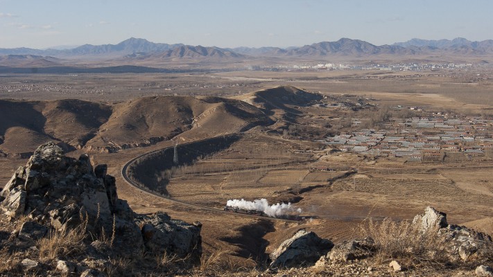 Two QJ steam locomotives lead a westbound Jitong Railway freight train into Lindong, Inner Mongolia, China, in November 2005.