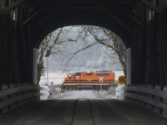 Portland and Western's Toledo Hauler freight train rolls east at Harris, Oregon, framed by the covered bridge over the Marys River on the drab winter day of December 29, 2009.