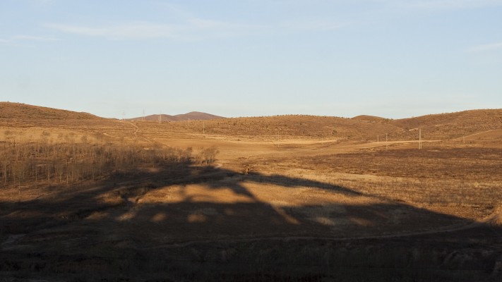 The morning sun casts a long shadow of two Jitong Railway QJ steam locomotives departing Daban, Inner Mongolia, China, in the fall of 2005.