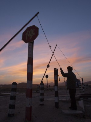 The Jitong Railway gatekeeper at Baomutu, Inner Mongolia, China, raises the crossing gates following the passage of a westbound train at twilight.