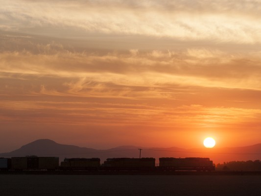 The setting sun touches the ridge of western Oregon's Coast Range mountains, silhouetting Union Pacific's Roseville to Portland Terminal freight train in the dusky harvest evening of August 14, 2008.