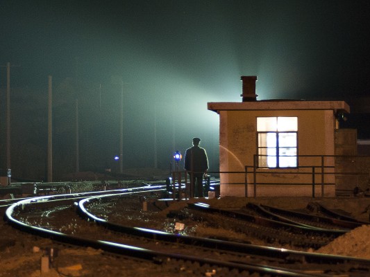 Lights from an arriving westbound train silhouette the switch tender and shanty in Daban, Inner Mongolia, China, on a fall night in 2005.