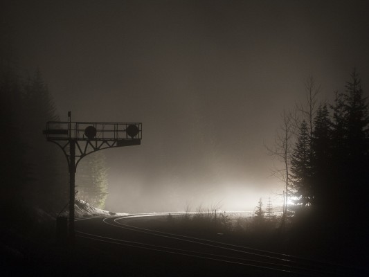 Lights from a southbound Union Pacific freight train illuminate the fog and silhouette the former Southern Pacific signal bridge at the south switch of Cruzatte siding on the evening of February 6, 2010, in the Oregon Cascades.