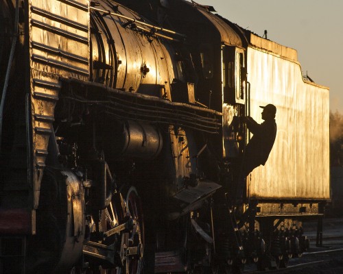 Jitong Railway worker climbing into the cab of a QJ steam locomotive at sunset in Daban.