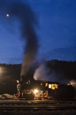 Smoke curls around a crescent moon in the predawn sky above Lixin, Heilongjiang, China, as a narrow-gauge 0-8-0 C2 steam locomotive of the Huanan Forestry Railway waits to take a loaded coal train west.