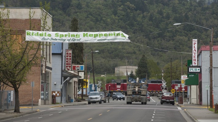 Central Oregon and Pacific freight train passing through Riddle, Oregon, as a log truck and other traffic wait on Main Street on April 19, 2010.