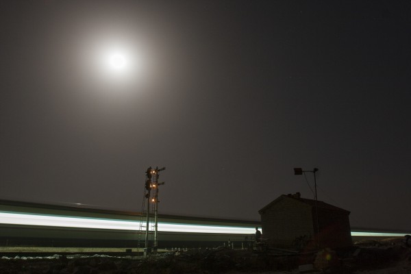 The Jitong Railway's diesel-powered streamlined passenger train passes a crossing shanty in Baomutu, Inner Mongolia, China, beneath the full harvest moon of October 2005.