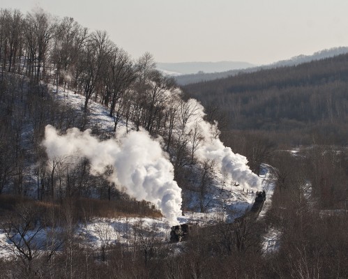 Two narrow-gauge 0-8-0 C2 steam locomotives pull and push an eight-car loaded coal train up the steep grade west of Lixin, Heilongjiang, China, on November 30, 2005.