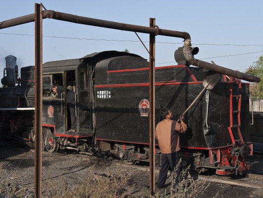 A worker of the Huanan Forestry Railway uses a shovel to position the water spout in Xiahua to replenish the tender of 0-8-0 C2 steam locomotive 168. The engine carries the well-worn tender of locomotive 043.