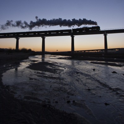 A single QJ steam locomotive leads a westbound Jitong Railway freight train across the tall viaduct near Chagganhada, Inner Mongolia, China, at dawn of a November day in 2005.