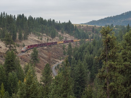 The St. Maries River Railroad's inbound Plummer Turn has just departed the Union Pacific interchange at Plummer, Idaho, with empty flatcars for the Potlatch Mill in St. Maries. The train is running on the former Milwaukee Road main line; visible below is the grade of Union Pacific's abandoned line to Wallace, Idaho, now a bike trail.