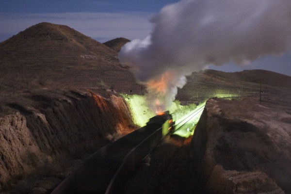 A westbound Jitong Railway freight train charges up the grade west of Tianshan, Inner Mongolia, China, on a moonlit night in November 2005. The orange glow on the steam comes from the open doors of the firebox as the fireman adds another shovel full of coal.