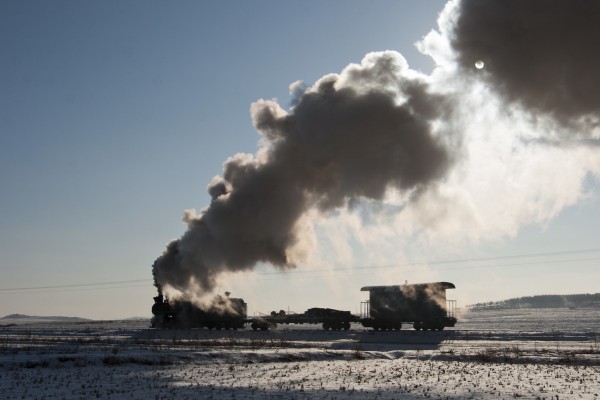 A work train steams east on the narrow-gauge Huanan Forestry Railway, en route to a derailed coal train near the summit on November 29, 2005. An 0-8-0 locomotive leads a flat car and caboose through the fields east of Huanan.