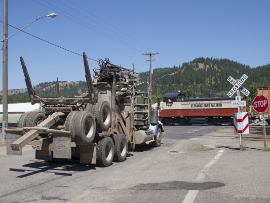 An empty log truck waits at the crossing in St. Maries, Idaho, while a St. Maries River Railroad SW1200 switches cars in the yard for an outbound Plummer Turn in July 2005.