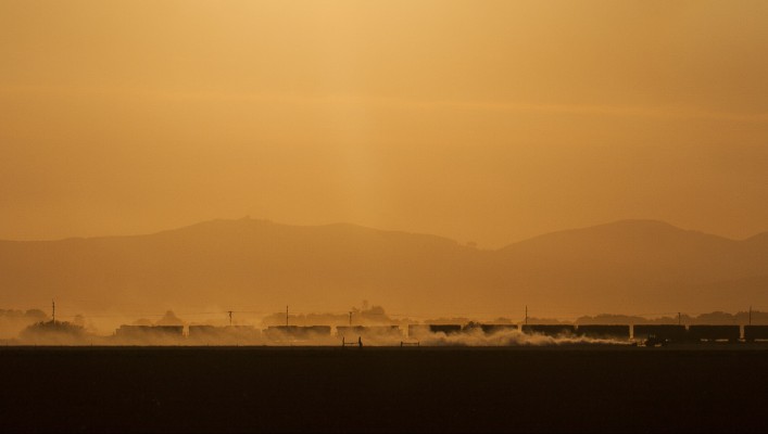 Late in the day of August 14, 2008, four Union Pacific locomotives lead Portland and Western's Eugene Hauler south as a tractor kicks up dust heading north through a field in the Willamette Valley near Harrisburg, Oregon.