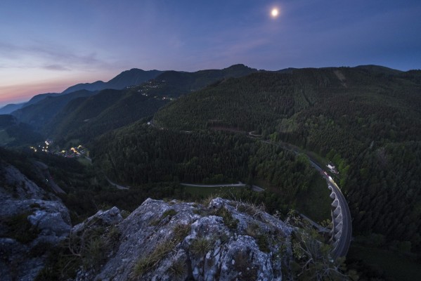 A waning moon hangs in the predawn sky above Breitenstein as a northbound freight train rolls onto the Kalte Rinne Viaduct. At far left, a green signal beckons the train onward, beneath the lights of the village.