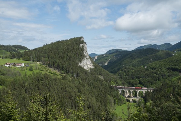 After a morning of showers and mist, the afternoon sun bathes Kalte Rinne Viaduct and the Polleroswand as a southward freight train of new automobiles heads upgrade with a Class 1142 headend helper leading a EuroSprinter locomotive.