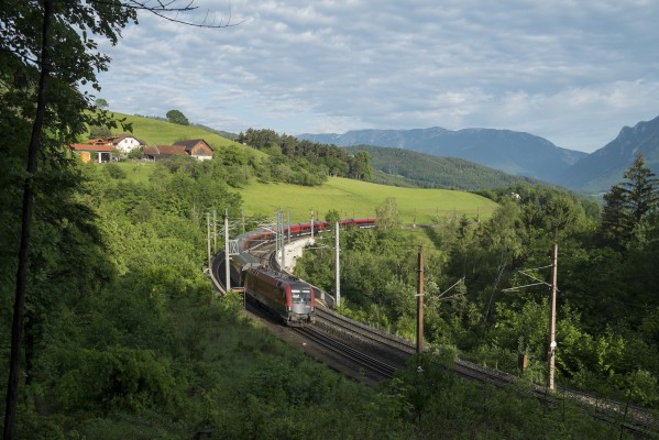 The day’s first Railjet passenger train, no. 551 for Graz, heads upgrade through rolling farmland near Eichberg as clouds scatter.