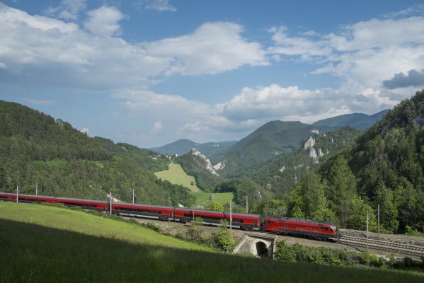 Vienna-bound Railjet passenger train rolling downgrade near Klamm; the 12th-century castle is visible in the distance near the center of the image. Railjet trains are configured for bidirectional operation; the locomotive is at the rear of this train.