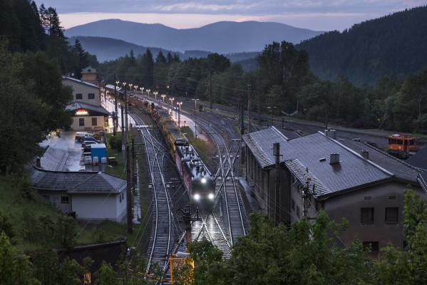 A pair of Class 1144 electrics leads a freight train through a light drizzle and into the summit tunnel at Semmering as twilight falls on a stormy day.