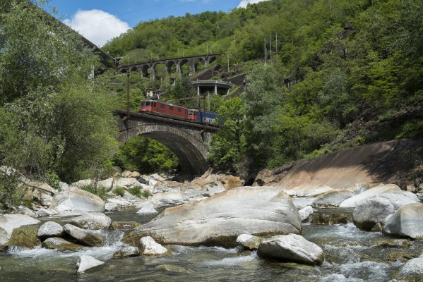 Two Swiss electrics lead an intermodal train south over the Ticino River at Biaschina. Two additional levels of track are visible behind the train, connected by the Piano Tondo and Travi spiral tunnels.