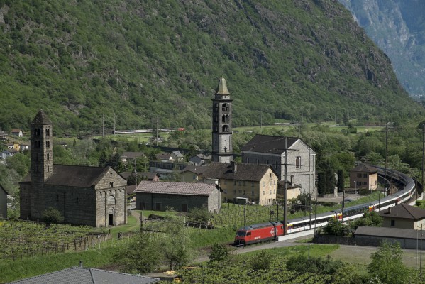 InterRegio passenger trains slide past one another at Giornico, Switzerland, on the southern approach to Gotthard Pass. With heavy passenger traffic on a holiday weekend, 8,000-horsepower Re 460 locomotives built in the mid-1990s handle both trains.