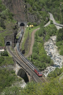 InterRegio passenger train crossing the Polmengo Viaduct over the Ticino River near Faido, Switzerland. The train has just exited the Prato Tunnel, one of four spiral tunnels on the southern ramp of Gotthard Pass, and is passing the short Boscerina Tunnel on the adjacent track.