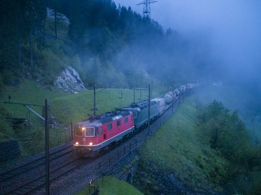 A container train climbs southward on the highest level track at Wassen, Switzerland, on a foggy May evening in 2016. The trailing Re 620 locomotive still wears its original green paint.