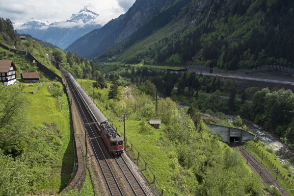 An InterRegio passenger train heads south near Wassen; having traversed the track at lower right and passed through the Pfaffensprung spiral tunnel. In the background, Chli Windgällen reaches a height of 9,797 feet.
