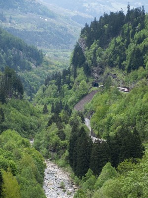 An ICN tilting passenger train runs high above the Ticino River just above Faido.