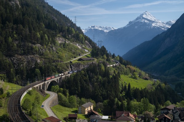 Swiss Federal Railways electric locomotives lead a container train down the middle level of track at Wassen, Switzerland, over the Middle Meienreuss Bridge with 9,797-foot Chil Windgällen in the background.