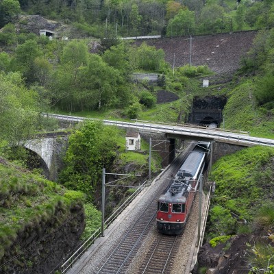 An InterRegio passenger train south exists the Freggio spiral tunnel and crosses the Ticino River.