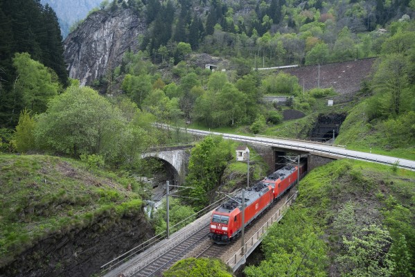 The same train from the previous view emerges from the Freggio spiral tunnel onto the lower level track, crossing the Ticino River in the Piottino Gorge.