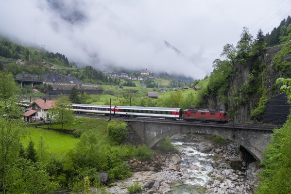 An InterRegio train south cross the River Reuss on the lower bridge at Wattingen. The famous 1733 church at Wassen is visible near the center of the image.