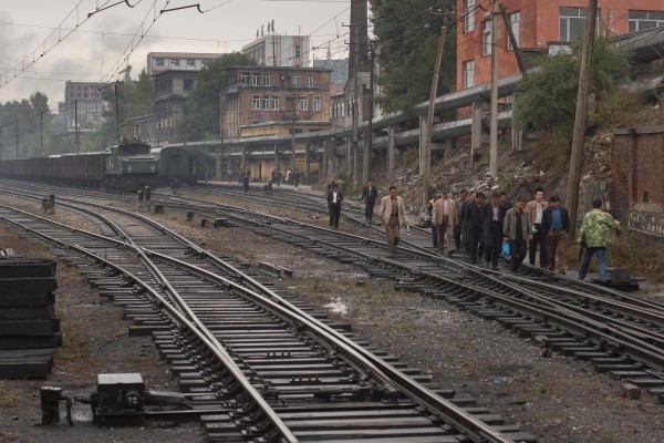 A group of men walk along the tracks in front of the passenger station at Hegang, China.