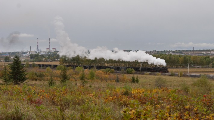 An SY-class 2-8-2 steam locomotive leads a coal train past a distant power plant on the Hegang Coal Mining Railway.