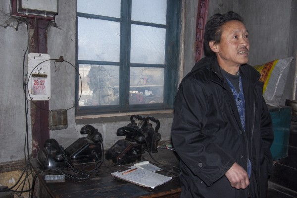 The station agent at Xiahua, Heilongjiang, China, on the Huanan Forestry Railroad on November 27, 2005, with a remarkable collection of telephones on his desk and a steam-powered coal train out the window.