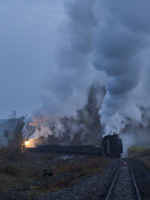 Two narrow-gauge 0-8-0 C2 steam locomotives pull and push an eight-car loaded coal train up the steep grade out of Lixin, Heilongjiang, China, just before dawn on September 29, 2005.