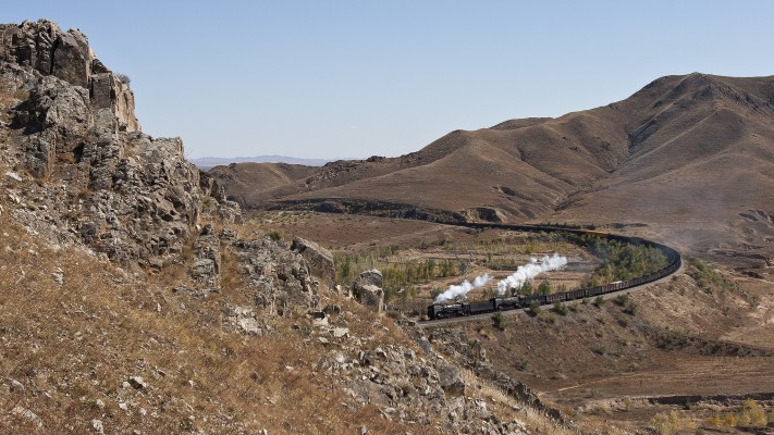 Westbound Jitong Railway freight train led by two QJ steam locomotives approaching LIndong, Inner Mongolia, China, though a sweeping curve on October 2, 2005.