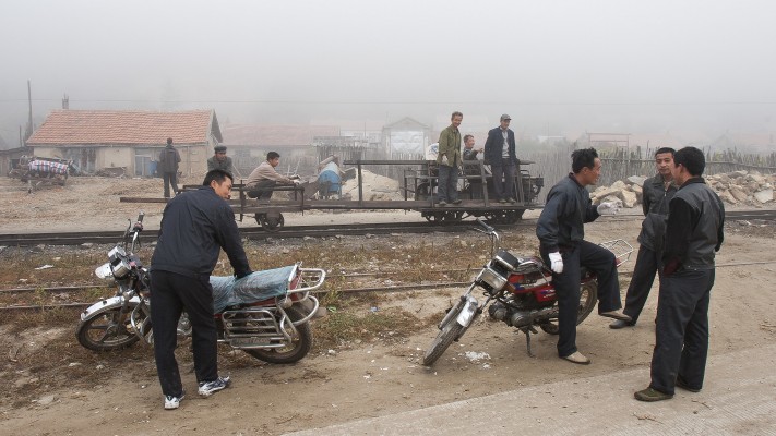 After the morning coal train passed through the village of Tuoyaozi, the section gang headed out on the main line to replace a rail. They travel in what appears to be a home-built speeder, pulling a cart with the rail. In the foreground are two of the bikers that had carried my photography group (<a href="http://www.farrail.com" rel="noreferrer nofollow">www.farrail.com</a>) over the summit of the railway earlier in the morning.