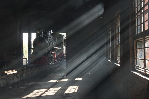 Sunlight filters through dirty air inside the enginehouse of the narrow-gauge Huanan Forestry Railway on September 28, 2005. Steam locomotive 21043, an 0-8-0 C2, rests just inside the door.